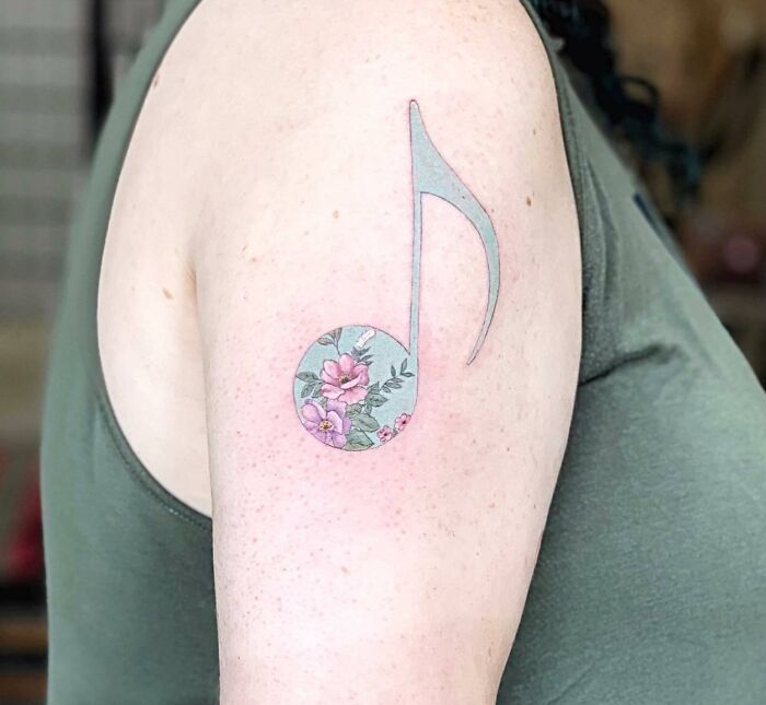 Floral music note tattoo on upper arm.