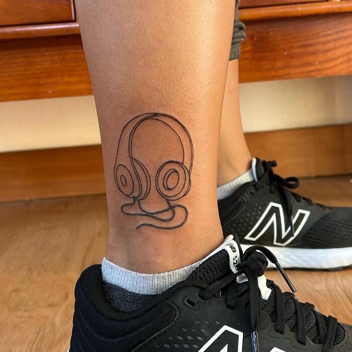 Outline tattoo of headphones on a calf, representing a love for music.