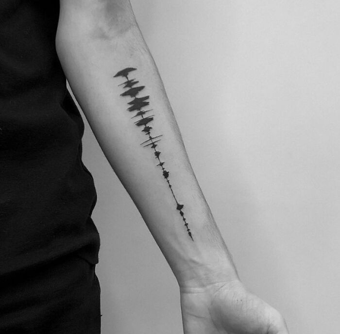 Forearm with a waveform music tattoo in black ink.