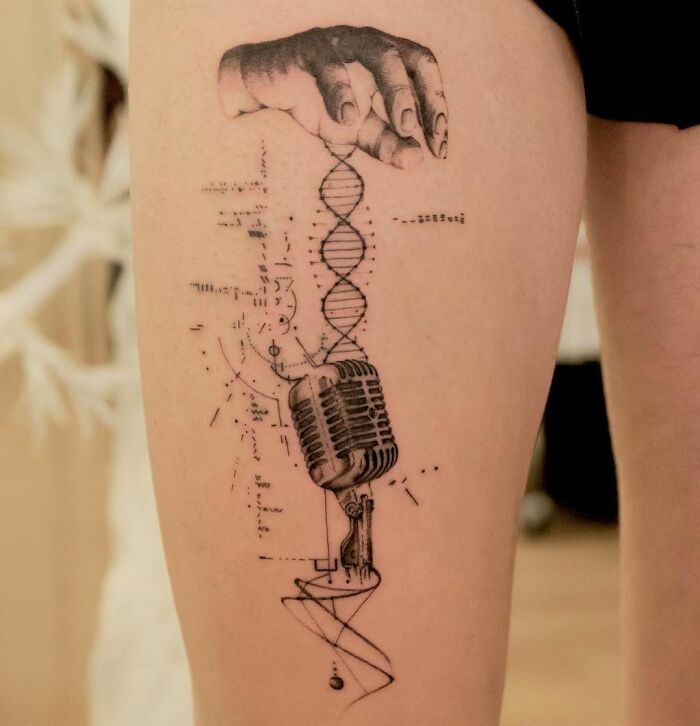 Intricate music tattoo featuring a vintage microphone and DNA design on the thigh.