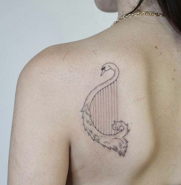 Tattoo of a swan as a harp on a person's back, symbolizing music.