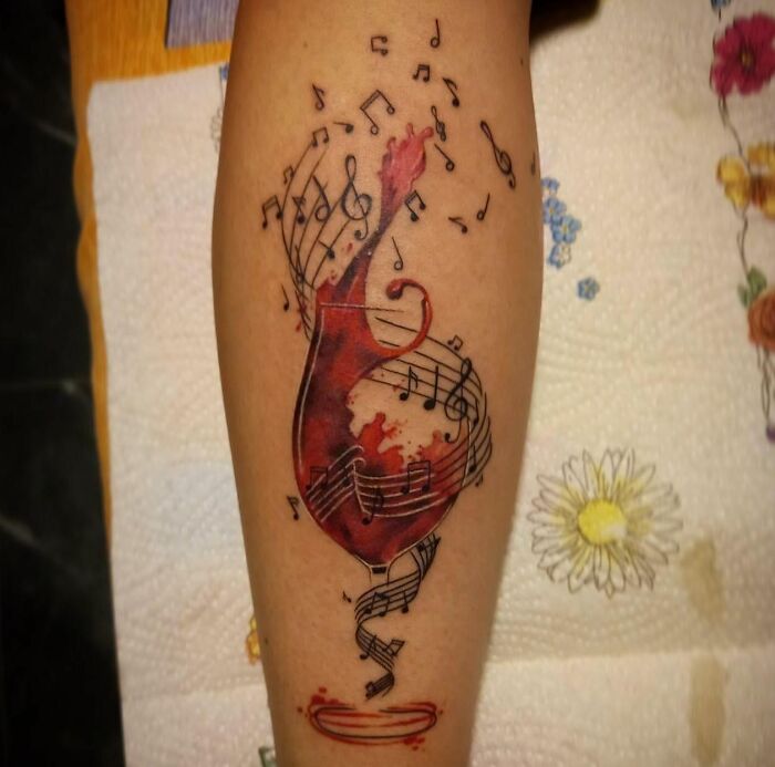 Tattoo of a vibrant red music note with flowing sheet music and notes, showcasing a unique music tattoo design.