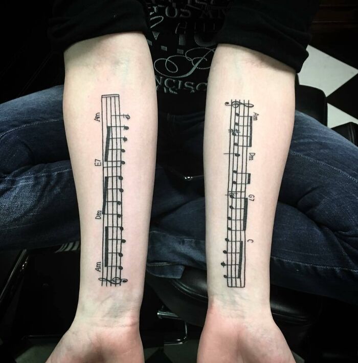 Music tattoos featuring sheet music inked on both forearms.