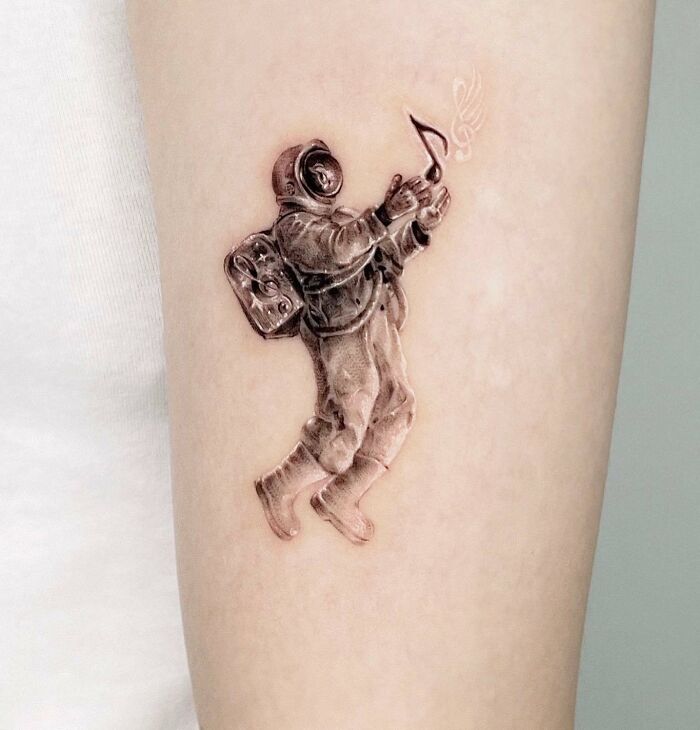 Astronaut holding a music note tattoo on arm, showcasing music tattoo artistry.