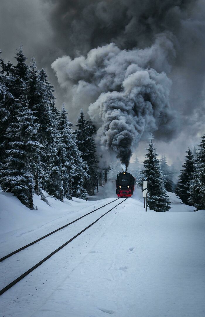 Steam train in snow-covered forest, emitting thick smoke; incredible world photos.