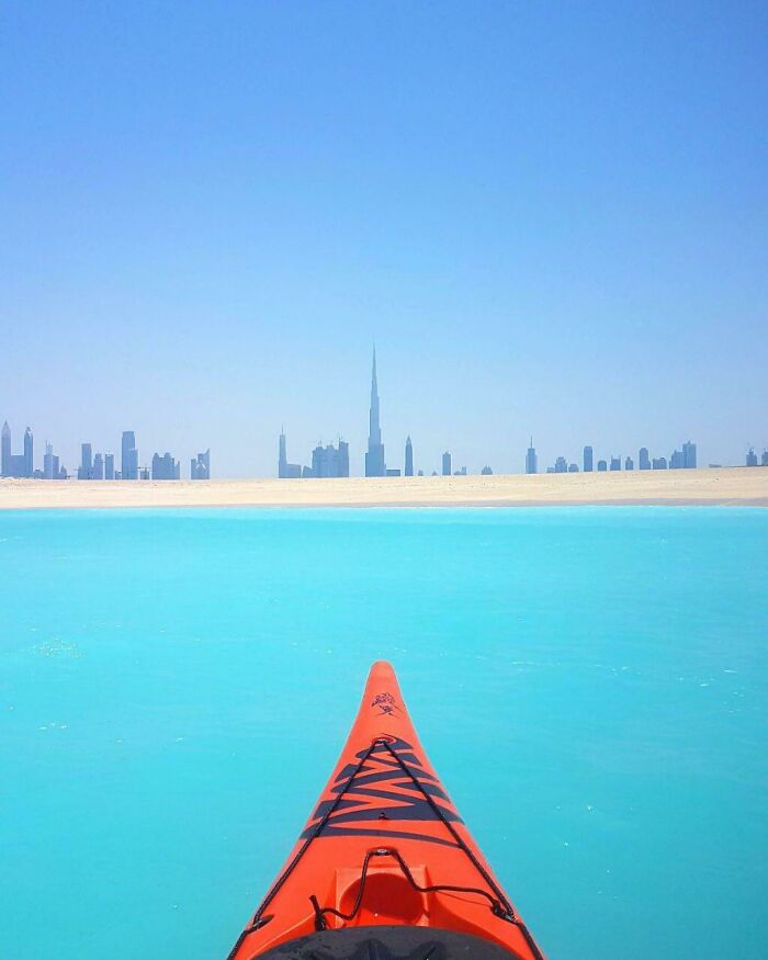 Orange kayak on turquoise water facing a distant city skyline; incredible world photos.