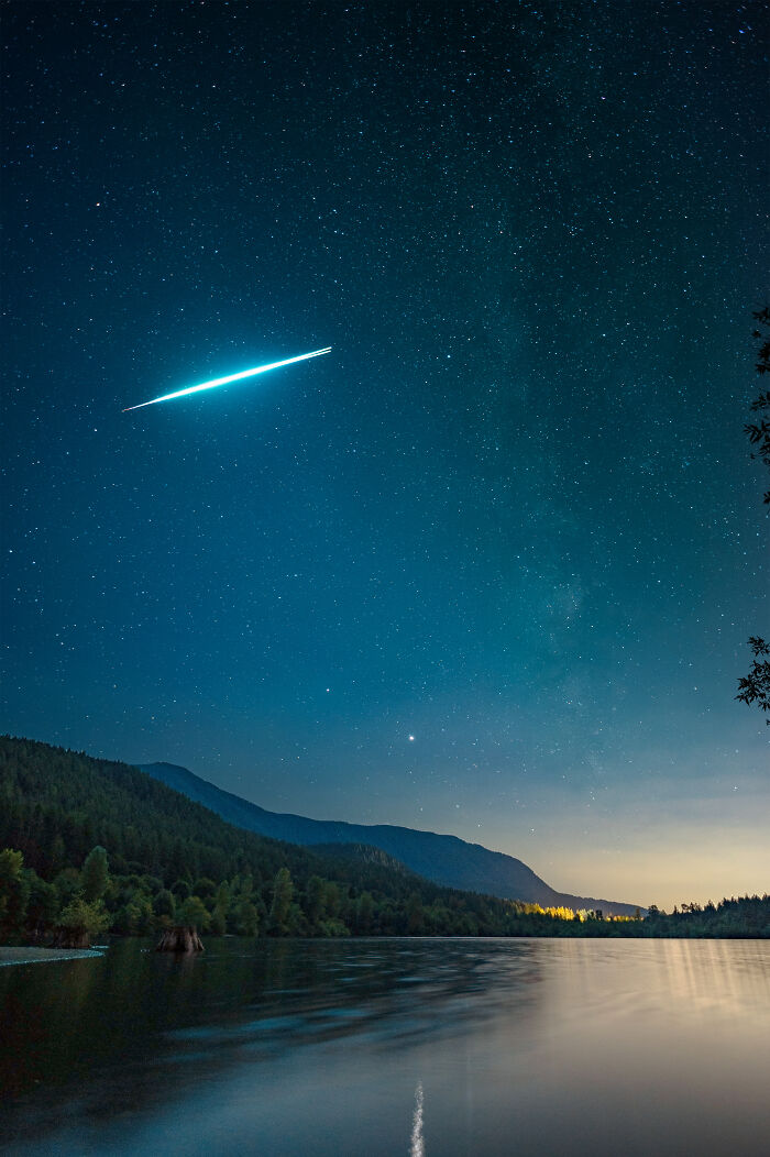 Starry night sky with meteor over a tranquil lake, showcasing incredible world photos.