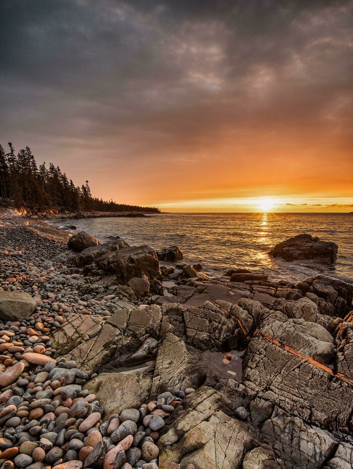 Sunset over rocky shore with calm ocean waves, capturing incredible world photos of a serene coastal landscape.