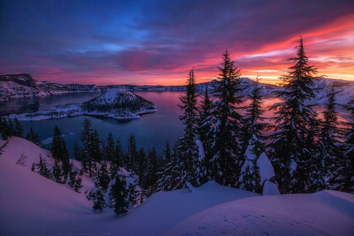 Incredible World Photos: Stunning sunset over snowy lake landscape with silhouetted pine trees.