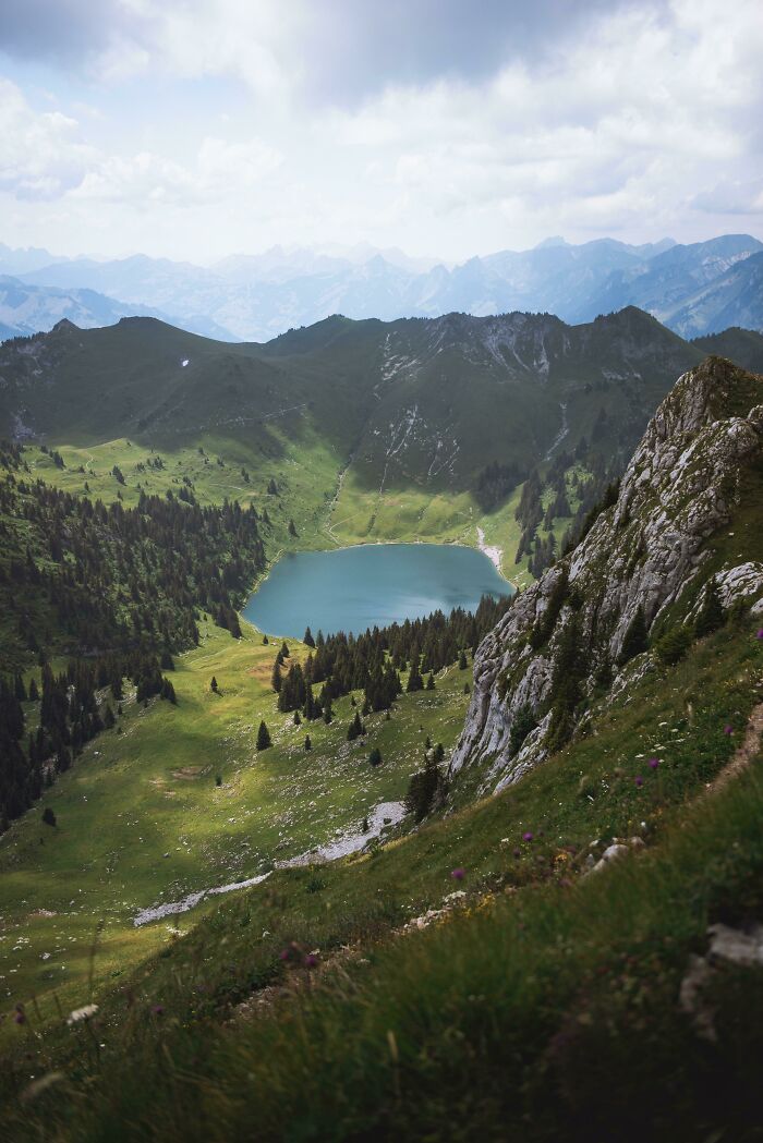 Incredible world photo of a serene mountain lake surrounded by lush greenery and rugged peaks under a cloudy sky.