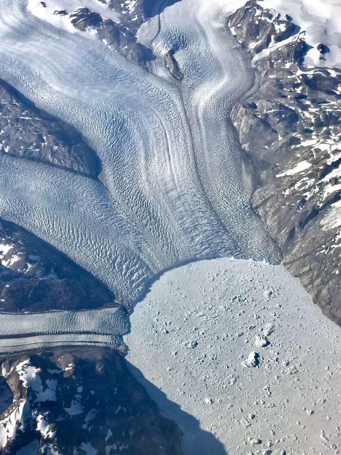 Aerial view of a stunning glacier flowing between snow-covered mountains, showcasing incredible world photos.