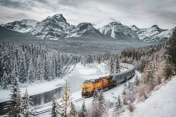 Train traveling through snowy mountains and forest, showcasing incredible world photos scenery.