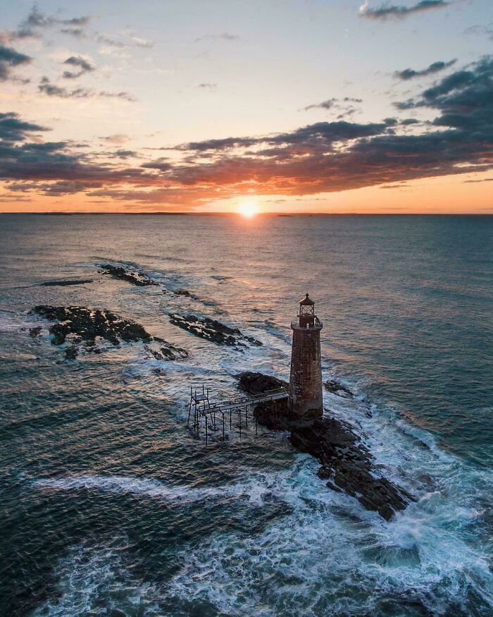 Lighthouse in the ocean at sunrise, dramatic clouds and waves in this incredible world photo.