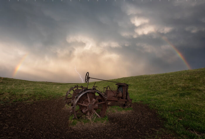 Old tractor in a field with a dramatic sky, rainbows, and lightning, part of incredible world photos collection.