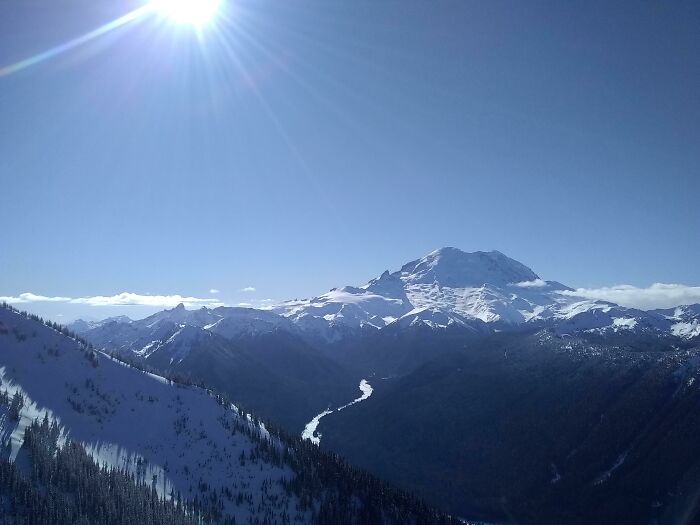 Snowy mountain peak under a clear blue sky with the sun shining brightly, showcasing incredible world photos.