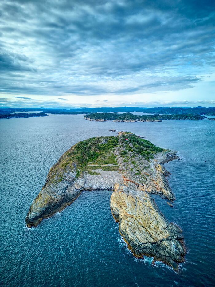 Aerial view of a rocky island surrounded by ocean under a cloudy sky, showcasing incredible world photos.