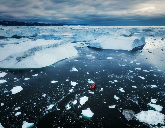 Incredible-World-Photos showcasing icebergs in a vast, icy ocean with a small red boat navigating the cold waters.