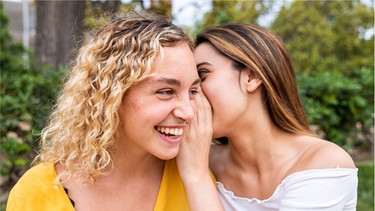 Eine junge Frau flüstert ihrer Freundin etwas ins Ohr. Komplimente machen glücklich, motivieren und stärken Beziehungen. Aber was ist ein gutes Kompliment? Unsere Tipps helfen euch dabei die richtigen Worte zu finden.
| Bild: Wochit/Getty Images