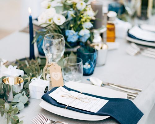 A wedding reception table design with floral arrangements, place settings, and glassware.