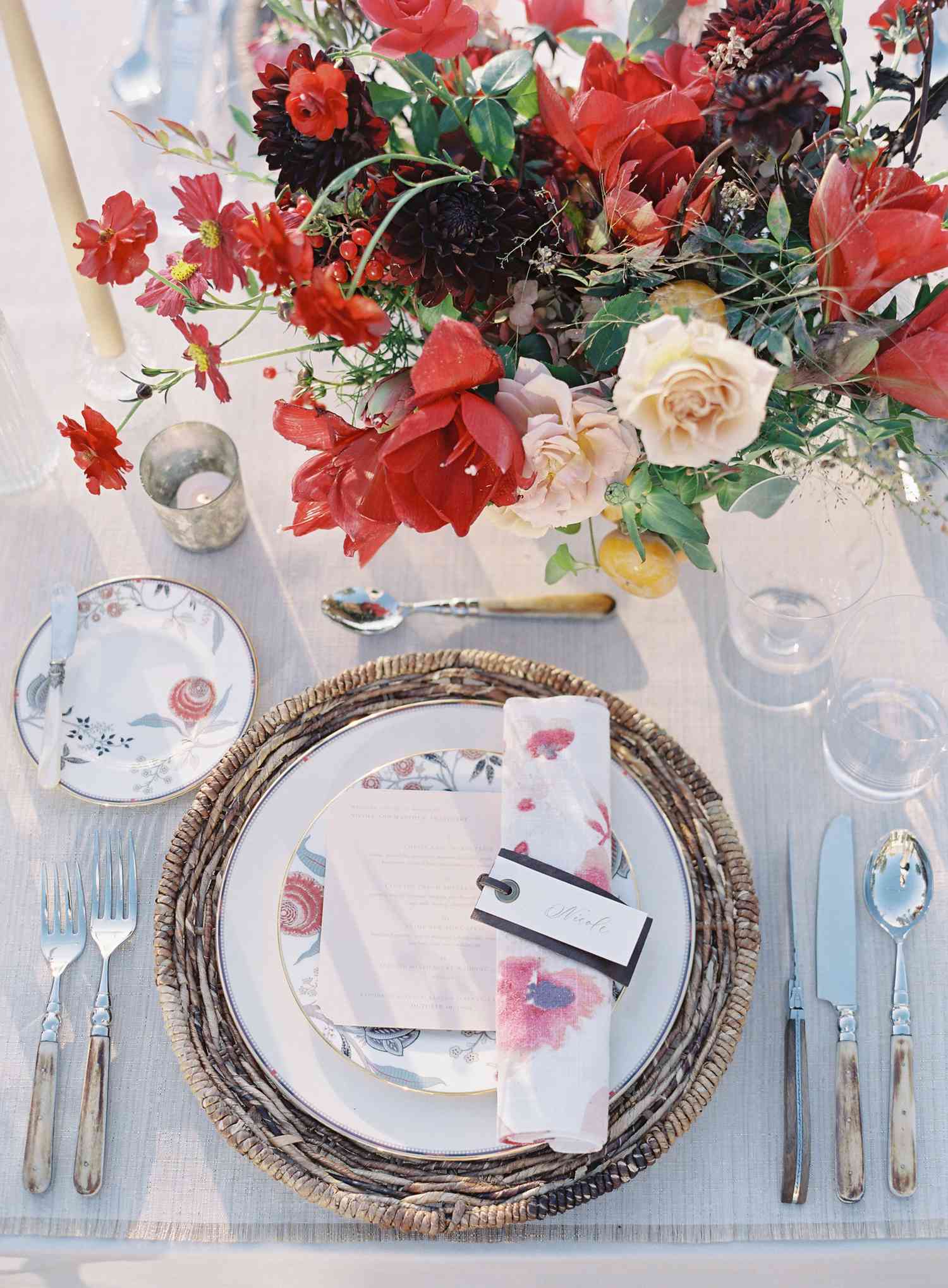 Tablescape with woven charger, floral china, floral napkins, and pink and red floral arrangements