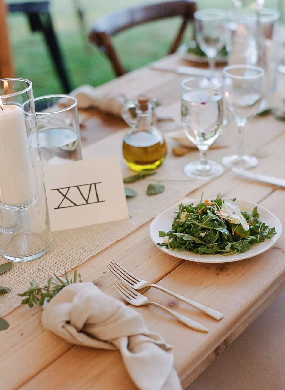Wood reception tables with natural linens, herbs, greenery, and roman numeral table numbers