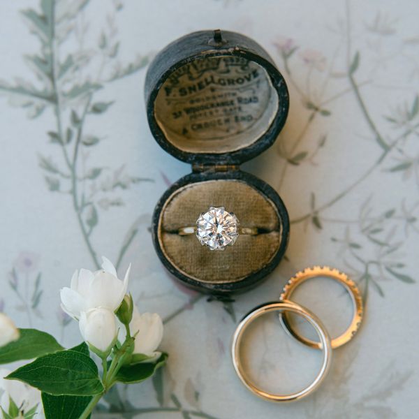 flat lay of an engagement ring in a ring box with two gold wedding bands on the side