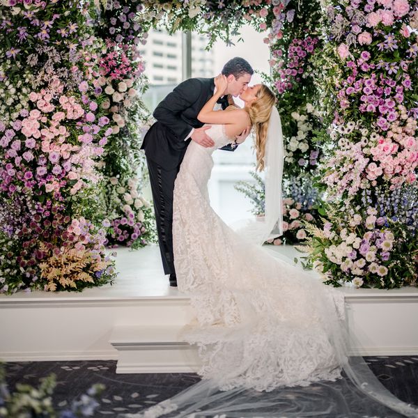 Bride in Strapless Wedding Dress and Veil Kissing Groom in Black Tuxedo at Altar With Colorful Flower Decor