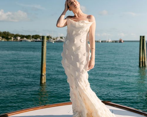 bride wearing a white maxi dress standing on a boat in front of an ocean view