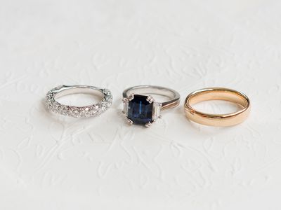 trio of rings: silver diamond wedding bands; silver sapphire and diamond three-stone engagement ring; gold wedding band