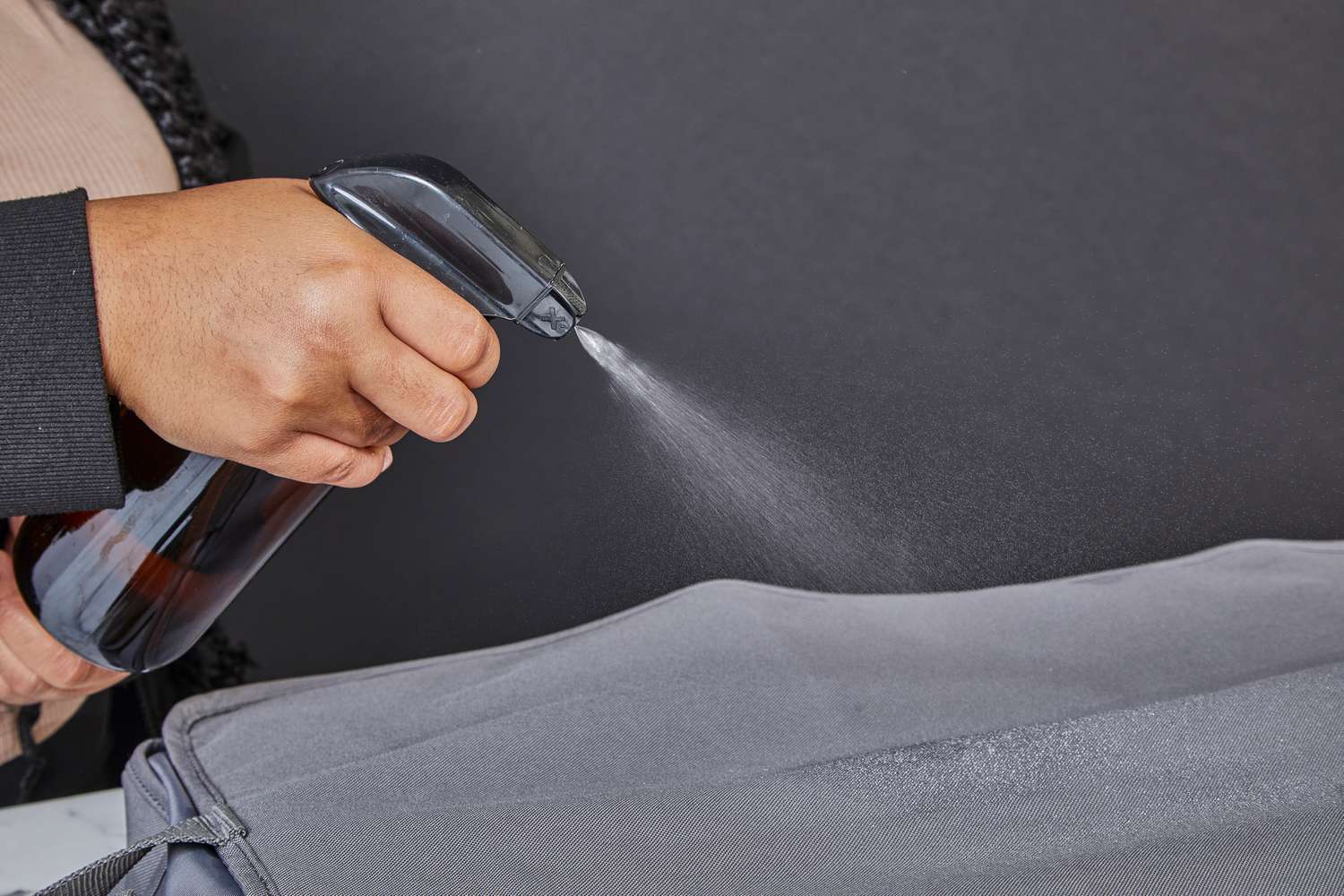 A closeup of a hand holding a spray bottle while spraying water on the WallyBags Deluxe Garment Bag