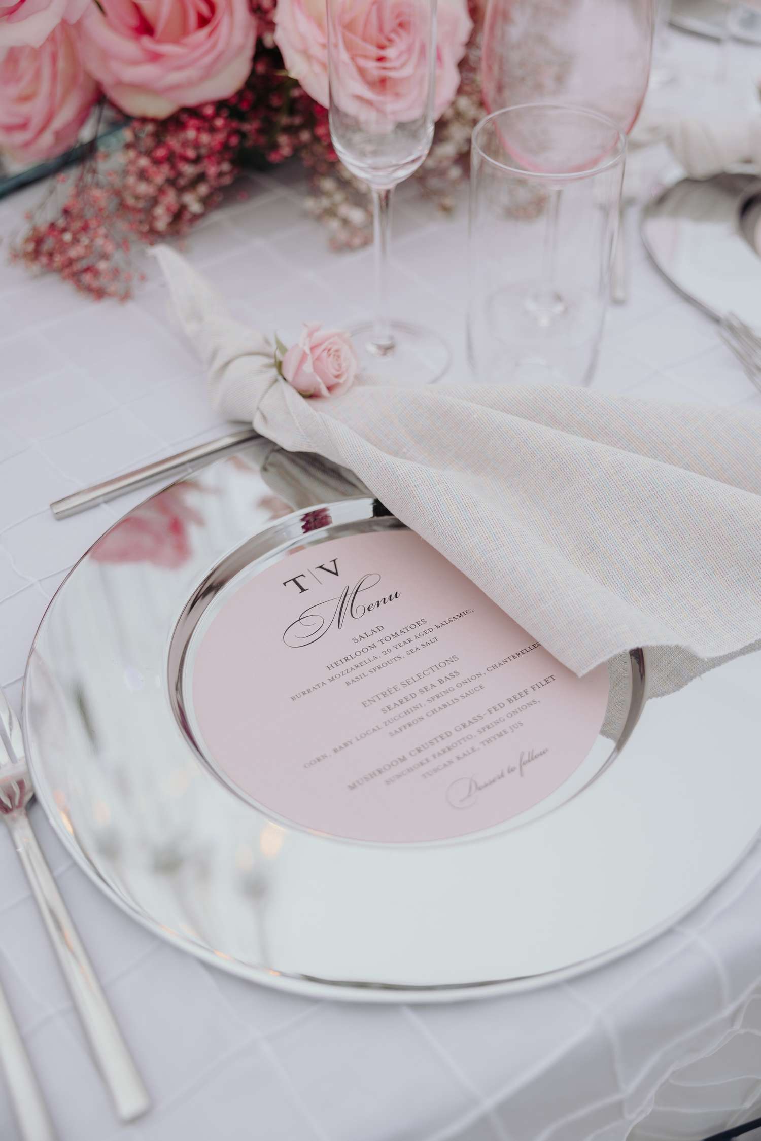 Place setting with mirrored charger, pink menu, and white linen napkin with rose