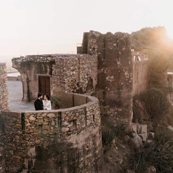 Bride in White Indian Wedding Dress Posing With Groom in Black Kurta on Stone Structure