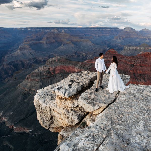 Bride and Groom Standing on Cliff Overlooking Canyon and Holding Hands