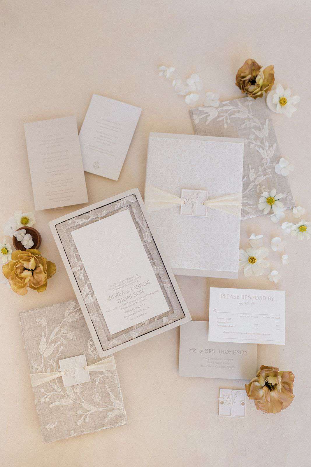 A linen boxed wedding invitation with white flowers.