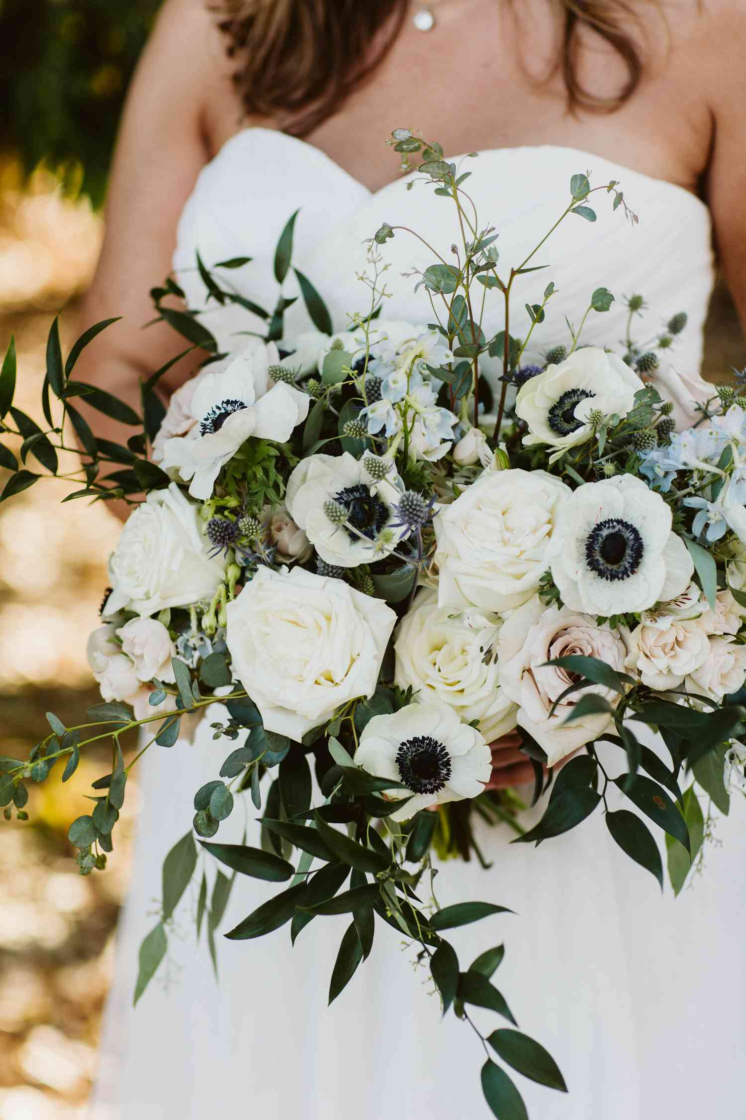 Bride holding a black and white floral bouquet with anemone, roses and greenery