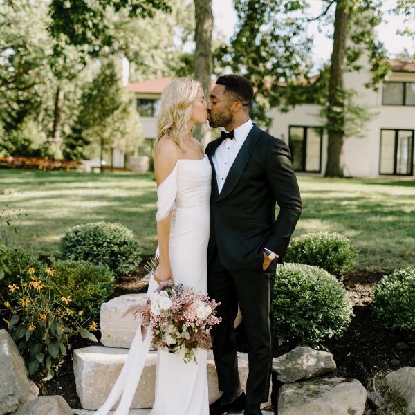 Bride and Groom Standing on Steps Outside of Home and Kissing