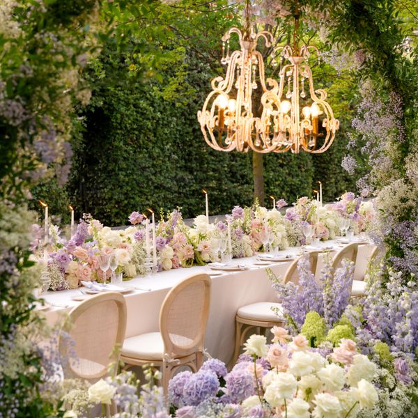 Wedding Reception Table Lined With Purple and White Floral Hedge and Floral Arrangement Surrounding It