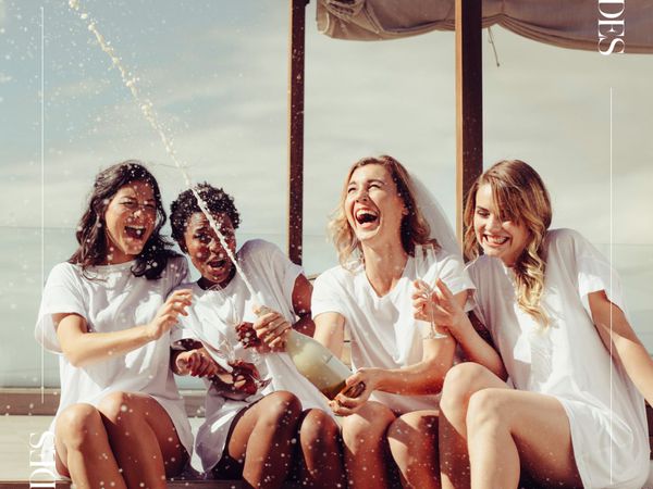 Bride popping a bottle of champagne with three women at a bachelorette party