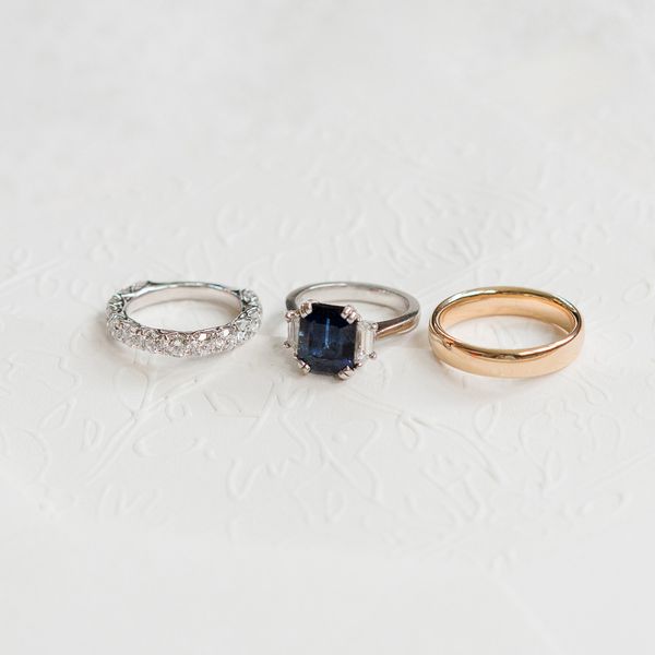 trio of rings: silver diamond wedding bands; silver sapphire and diamond three-stone engagement ring; gold wedding band