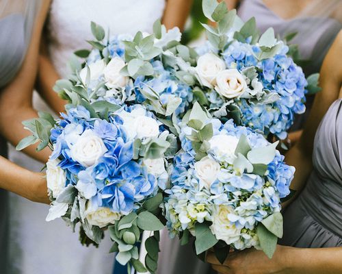 View of bride and bridesmaids holding blue and white flower bouquets during a wedding ceremony.