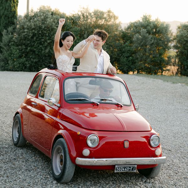 Bride in Strapless Wedding Dress and Groom in Tan Suit in Red Mini Fiat Car