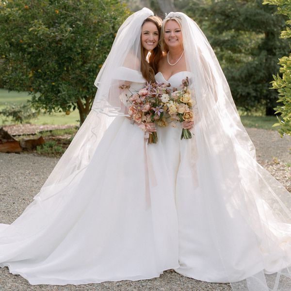 two brides wearing veils and holding pink, yellow, and peach bouquets