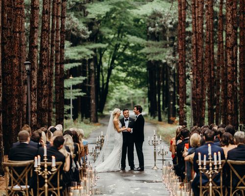 Bride and groom standing at the alter surrounded by candles, trees, and guests during a forest wedding ceremony.