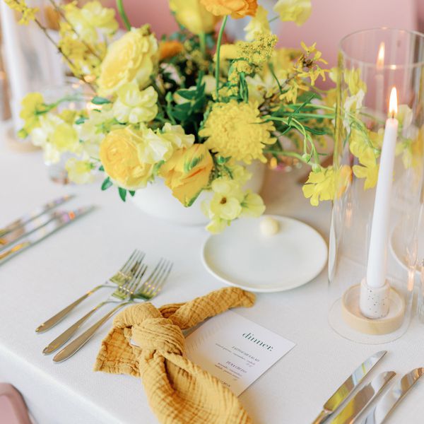 Tablescape with yellow floral centerpieces, white taper candles, and yellow knotted napkins