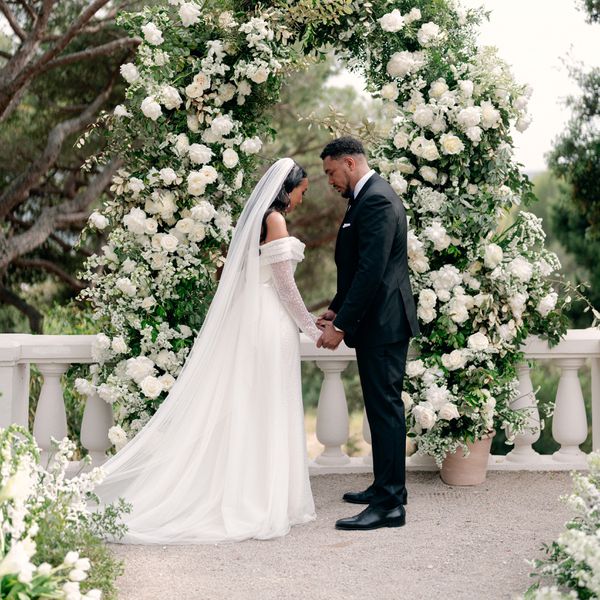 bride and groom holding hands in front a white rose ceremony altar arch