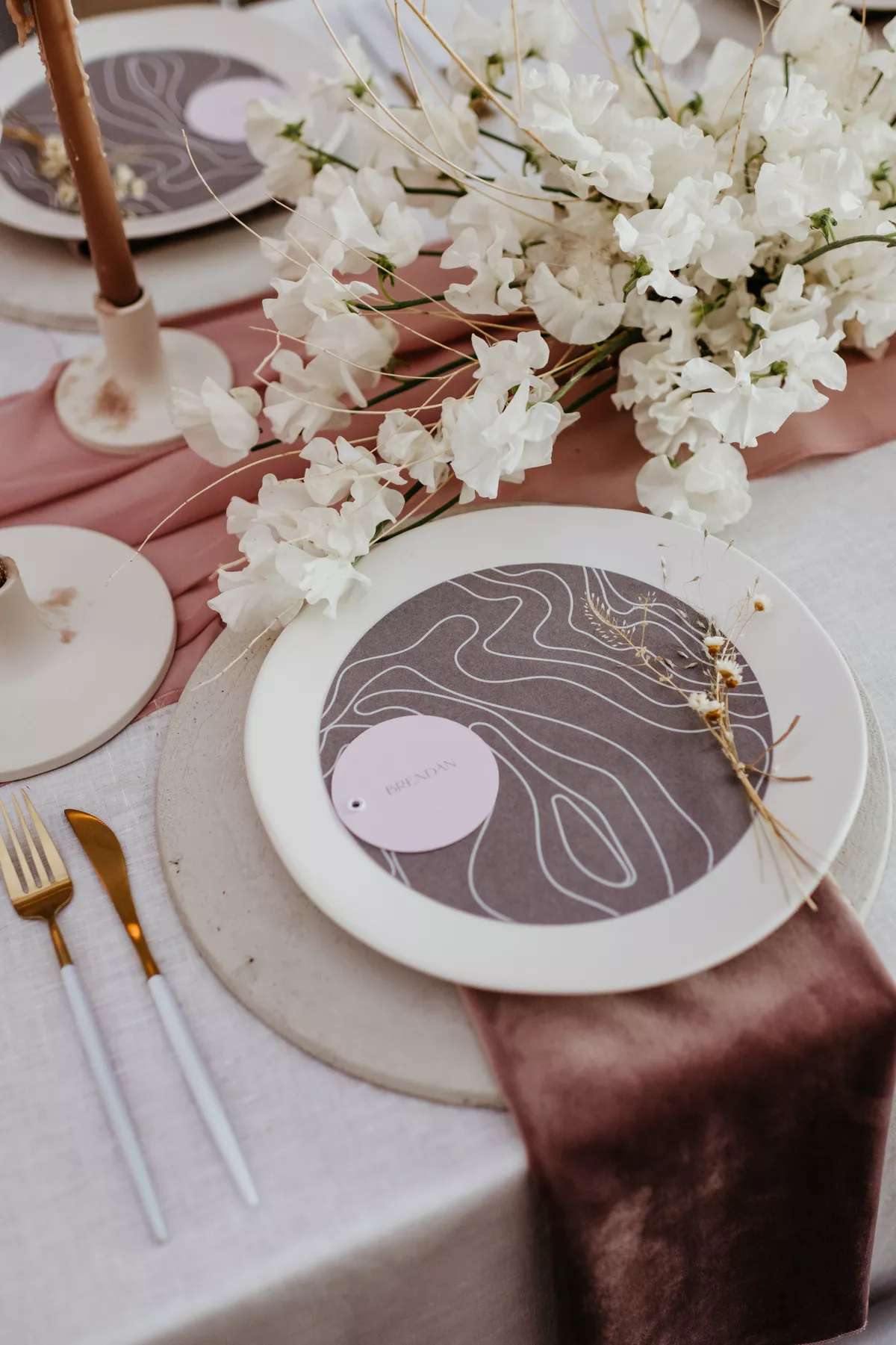 Bohemian tablescape with pink runner, white florals, candles, white plates, a purple menu design, velvet purple napkins, and ceramic plates