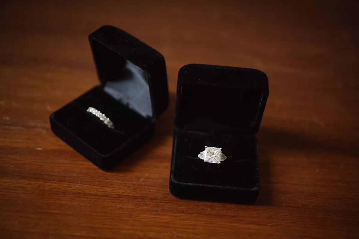 Princess cut engagement ring in black ring box and diamond wedding band in ring box beside it