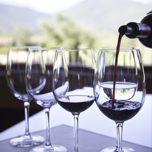 Red wine pouring into one of four wine glasses