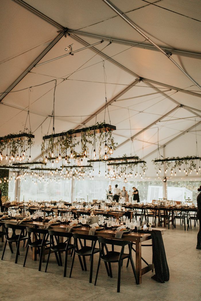 Black chandeliers with hanging bulbs and greenery over long wedding reception tables