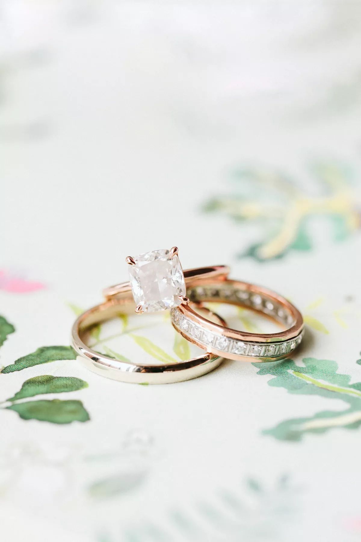 Cushion-cut engagement ring on rose gold band beside two wedding bands